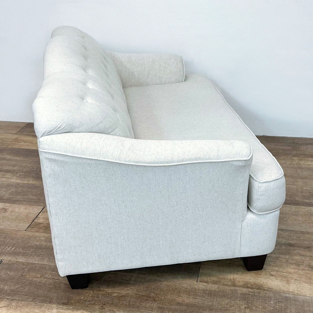 Side view of a tufted loveseat with dark finish feet on wooden floor.