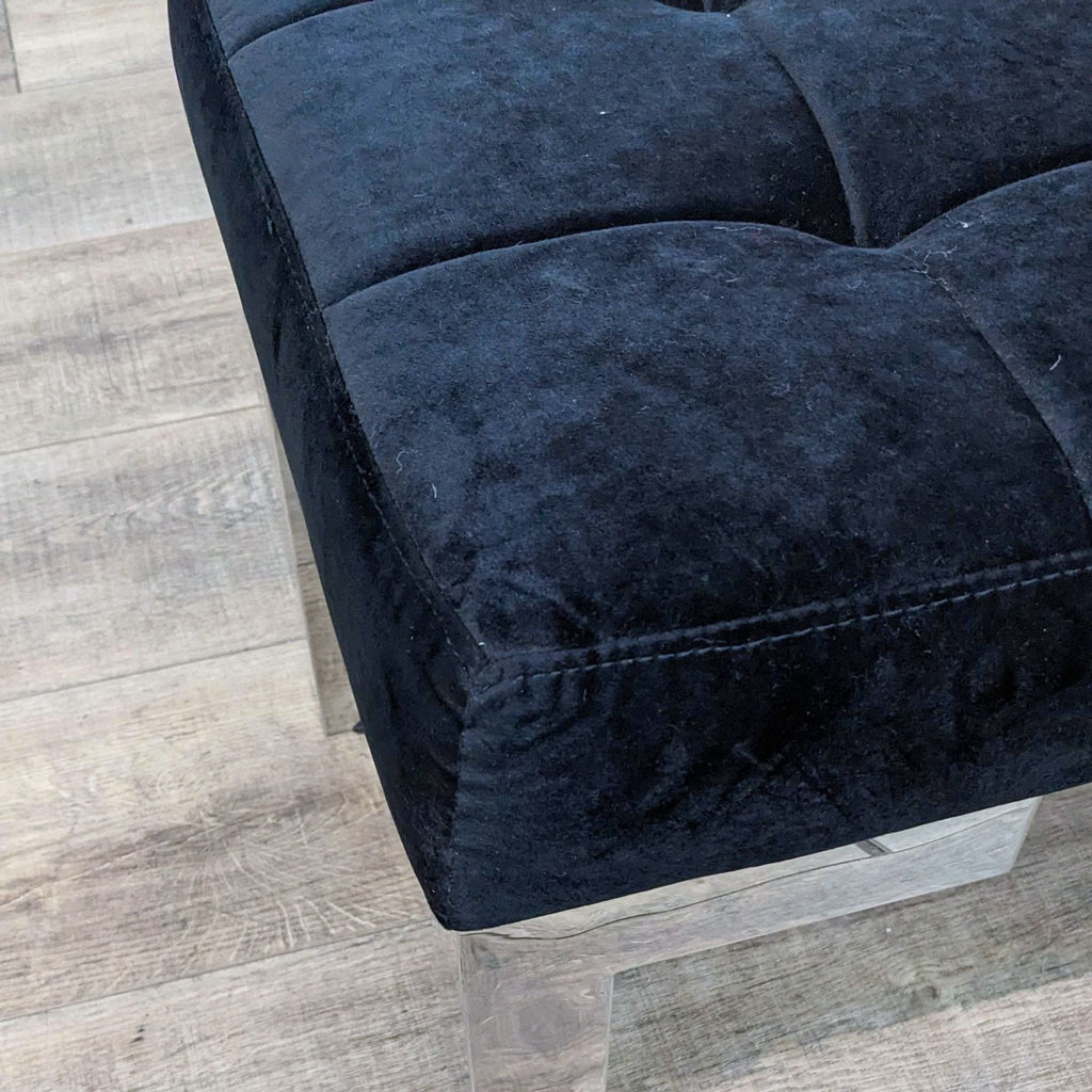 Close-up of black velvet tufted padding on a modern bench with chrome legs.