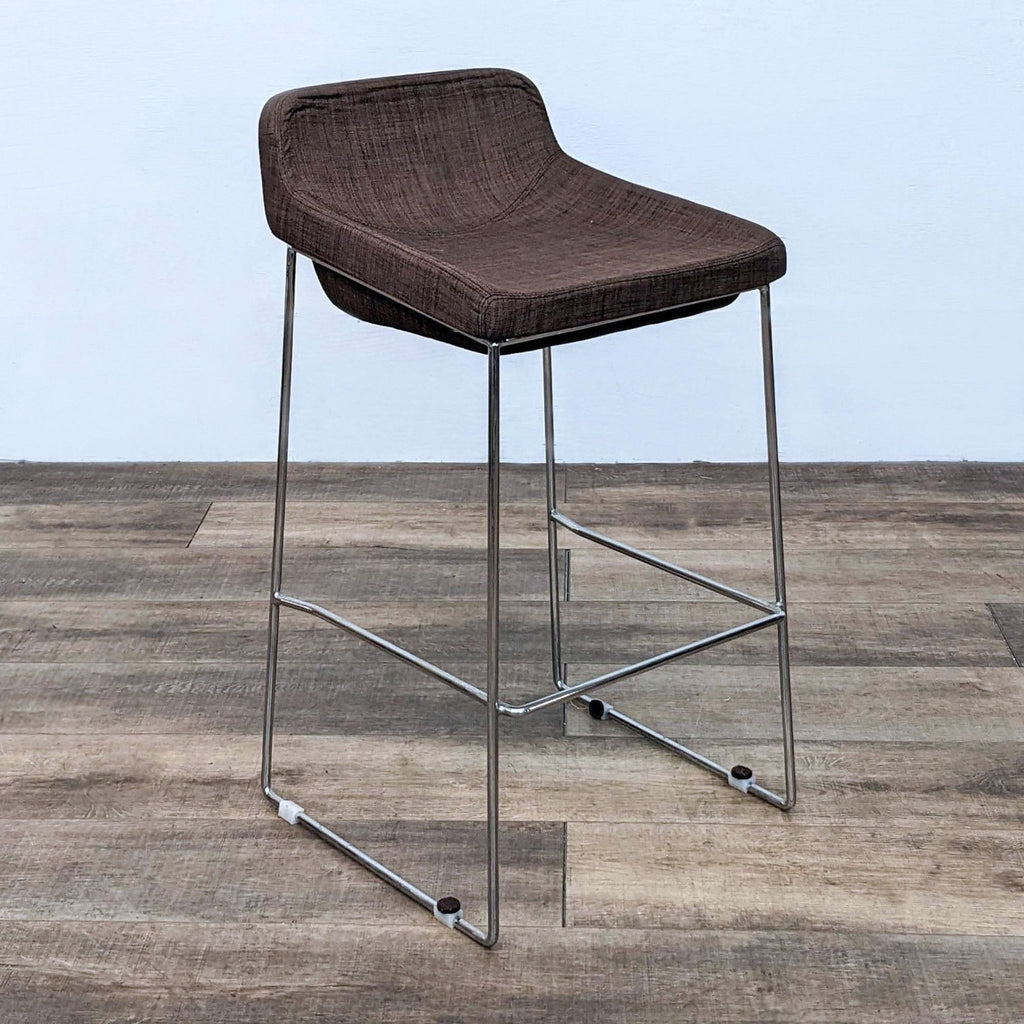 Side view of brown fabric stool with padded cushion and chrome frame, angled on wooden floor.