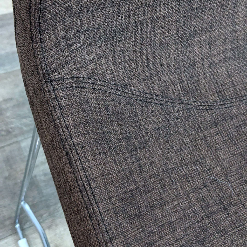 Close-up of brown fabric cushion texture on stool with chrome frame.