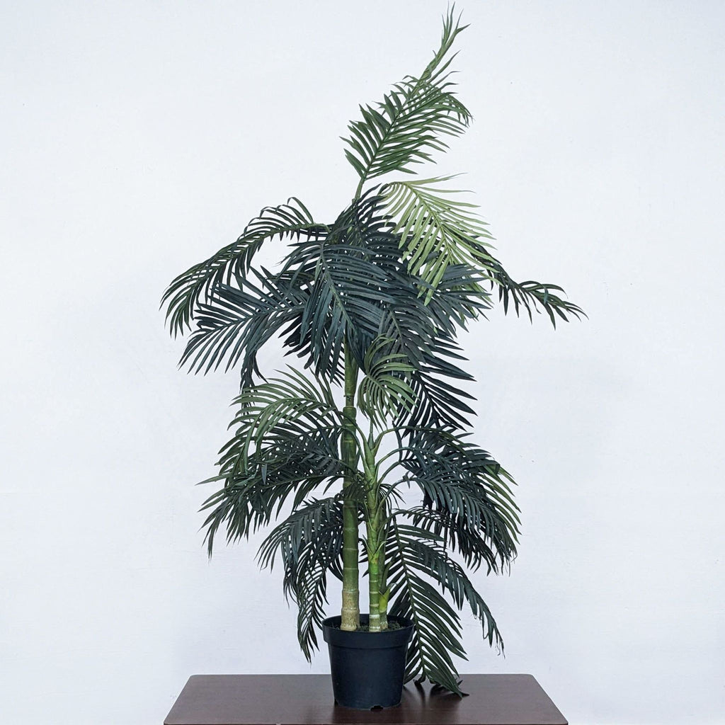 Faux bamboo plant in a black pot stands on a wooden surface.