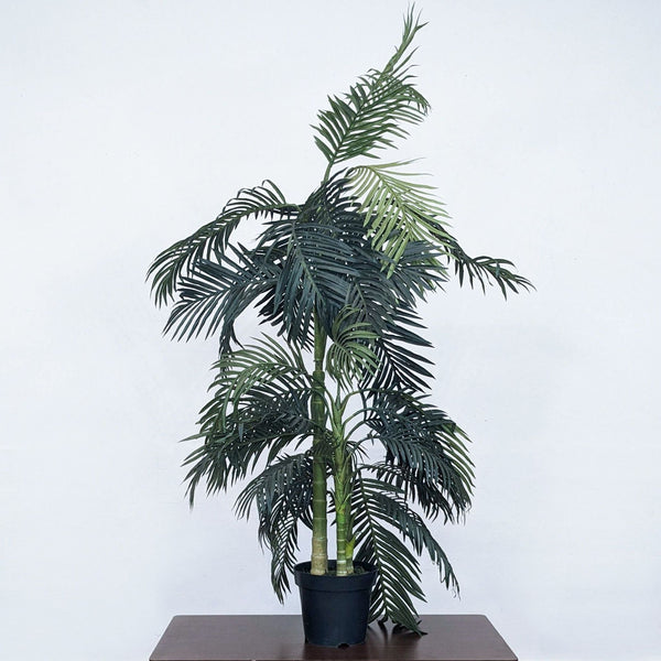 Faux bamboo plant in a black pot stands on a wooden surface.