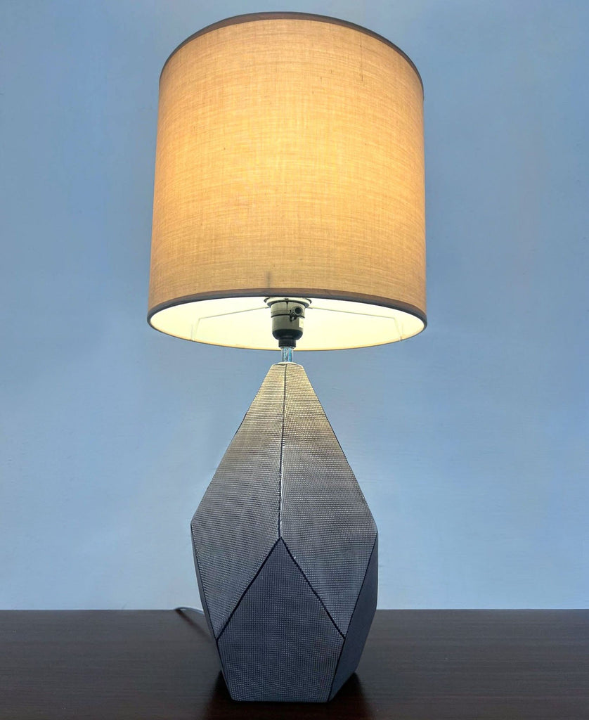 2. Reperch lamp illuminated, with beige shade casting a warm glow over its textured geometric base.  