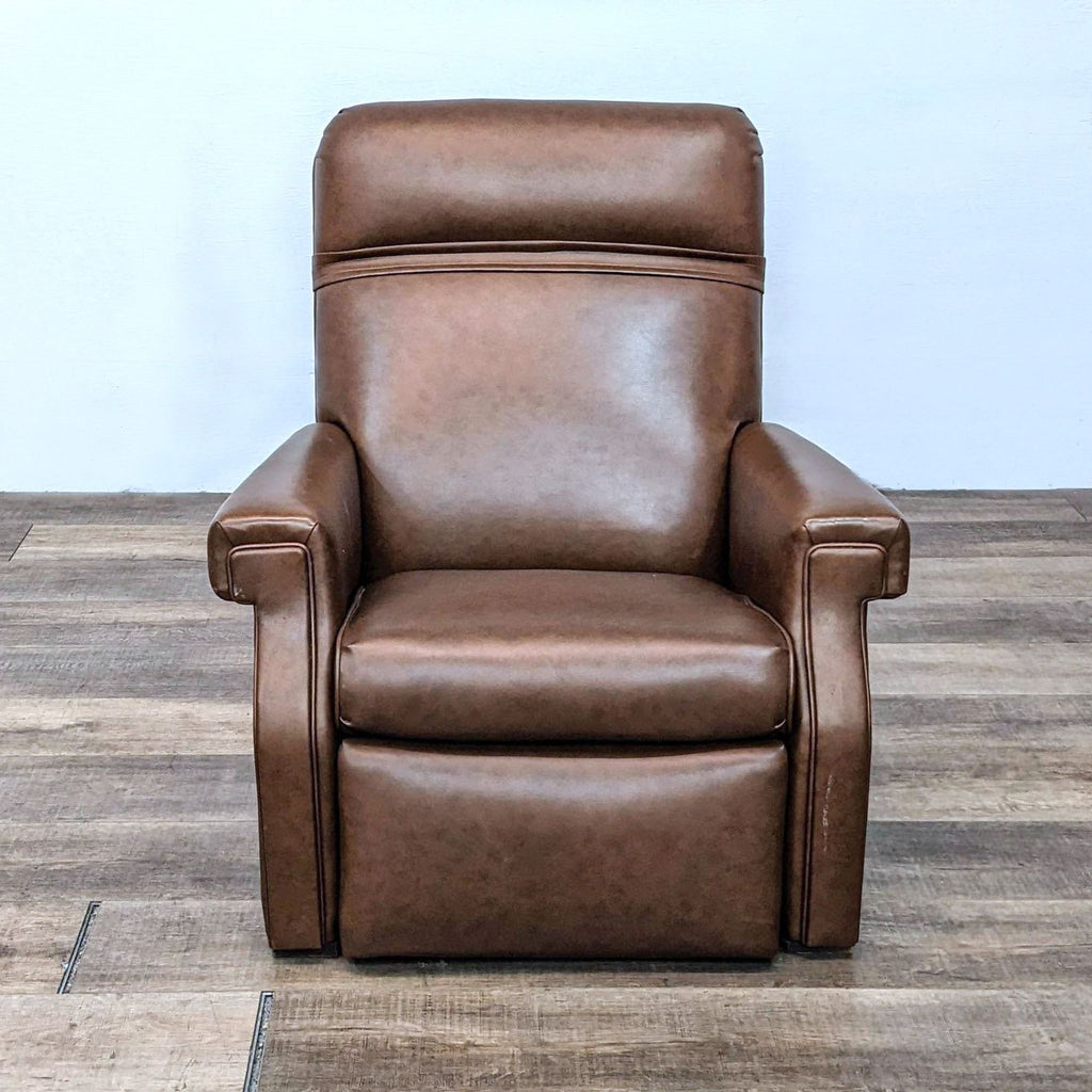 Brown leather recliner with nailhead trim, in upright position on wooden floor.