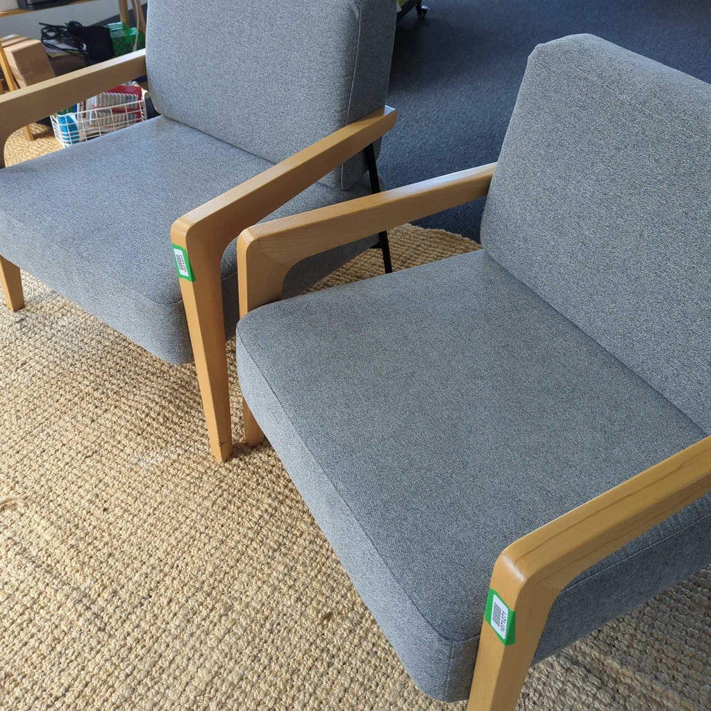 2. A pair of gray upholstered lounge chairs with light wood frames sit side by side on a beige woven rug.