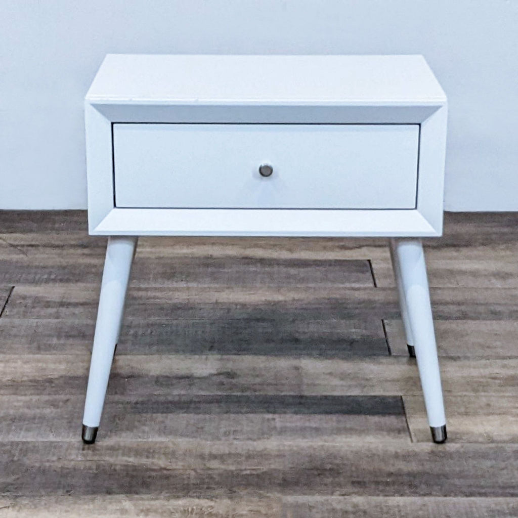 White end table with a single drawer, featuring sleek, angled legs and minimalist design.