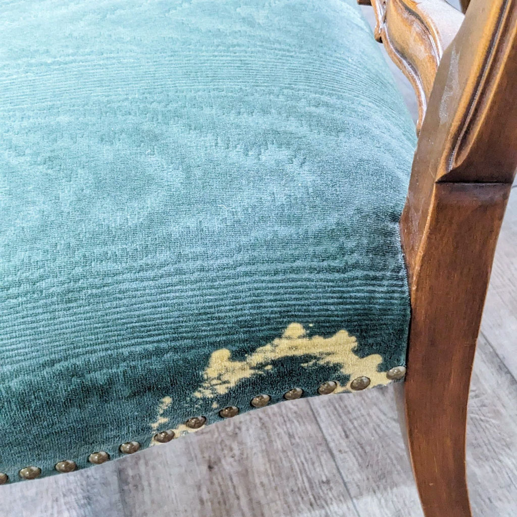 Close-up of upholstered chair with nailhead trim showing wear on the fabric.