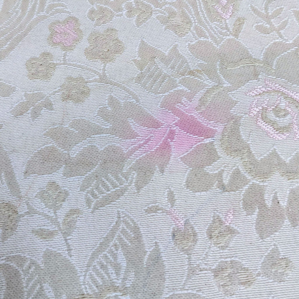 Close-up of floral damask fabric in beige tones with pink accents.