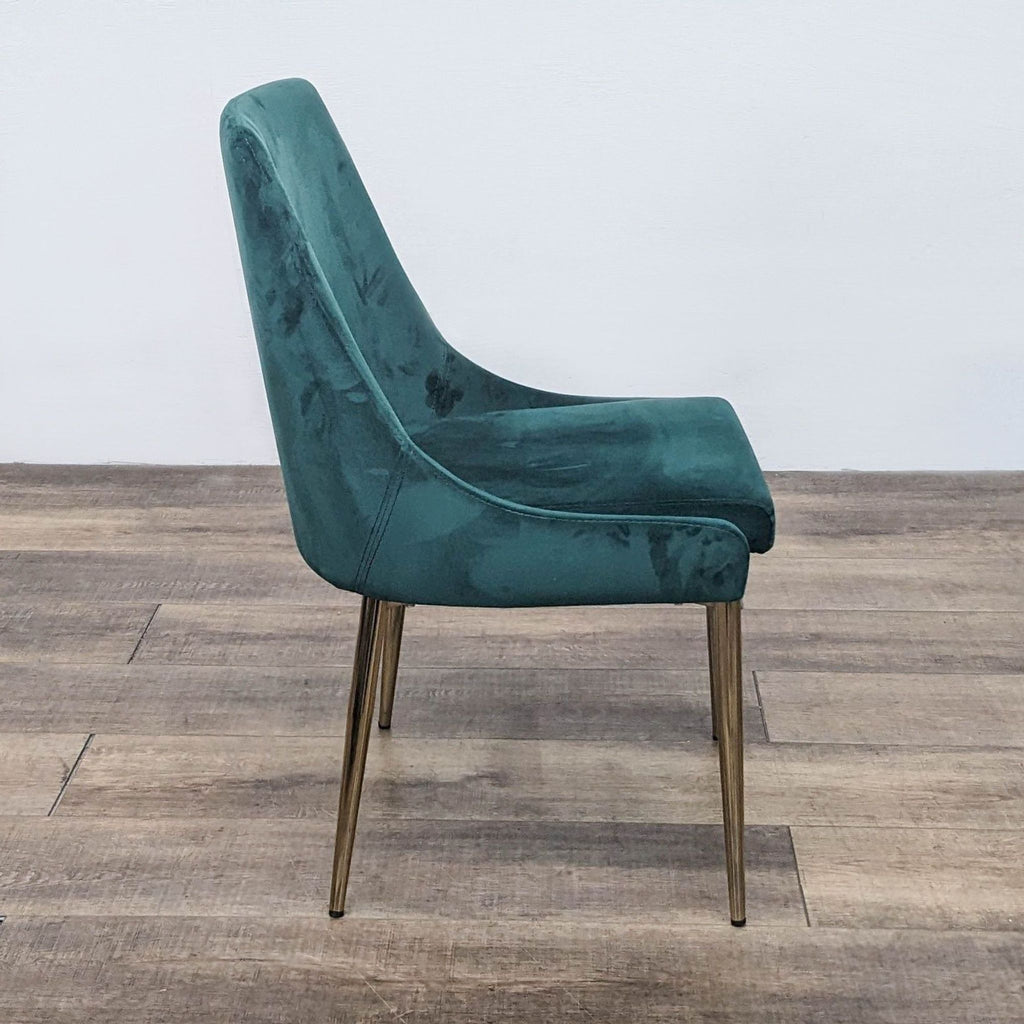 Side view of a green velvet chair with a sleek design and gold metal legs.
