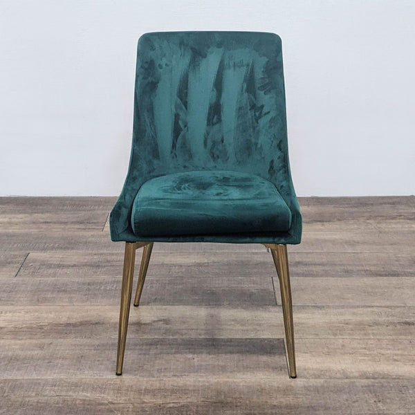 Front view of a green velvet dining chair with gold legs on wooden floor.
