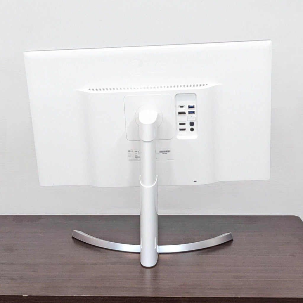 Back of LG monitor displaying multiple ports and a curved stand on a wooden desk.