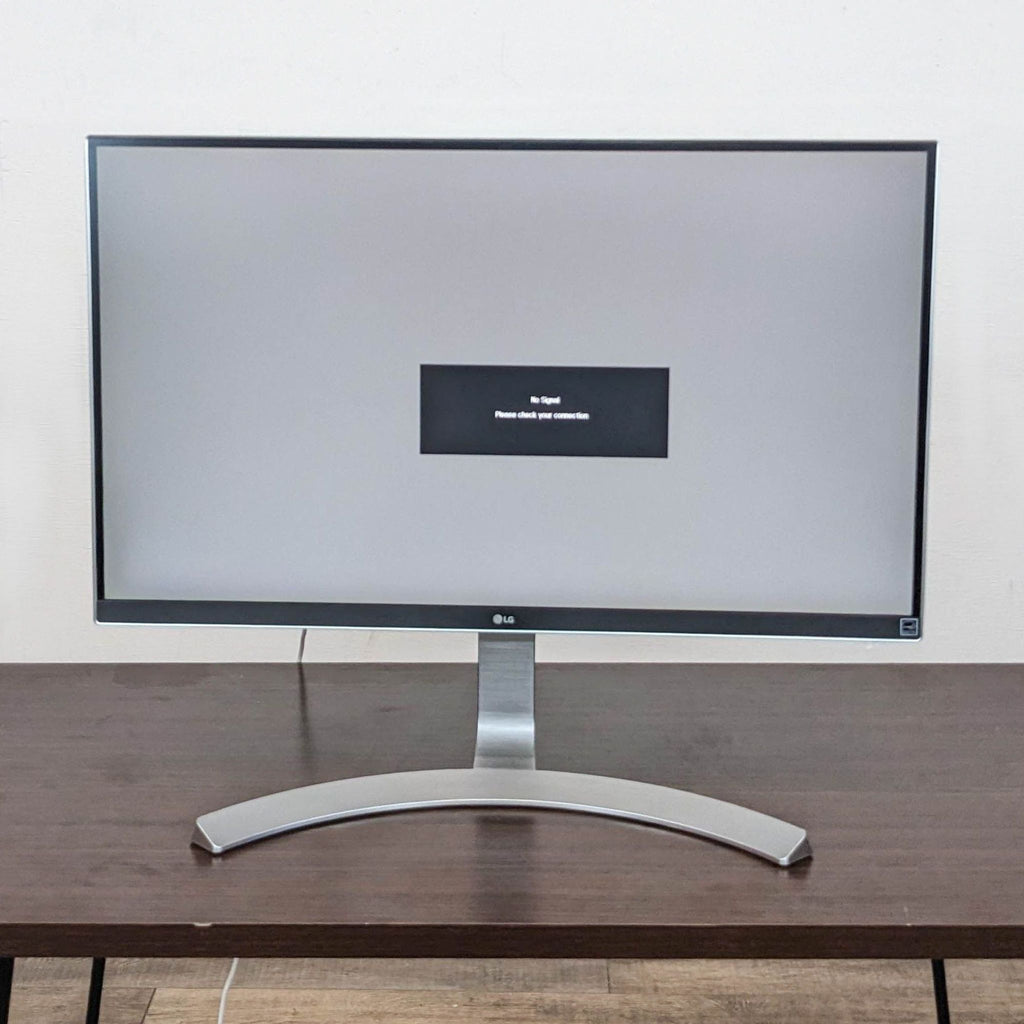 LG monitor with no signal message displayed on screen, set on a wooden desk.