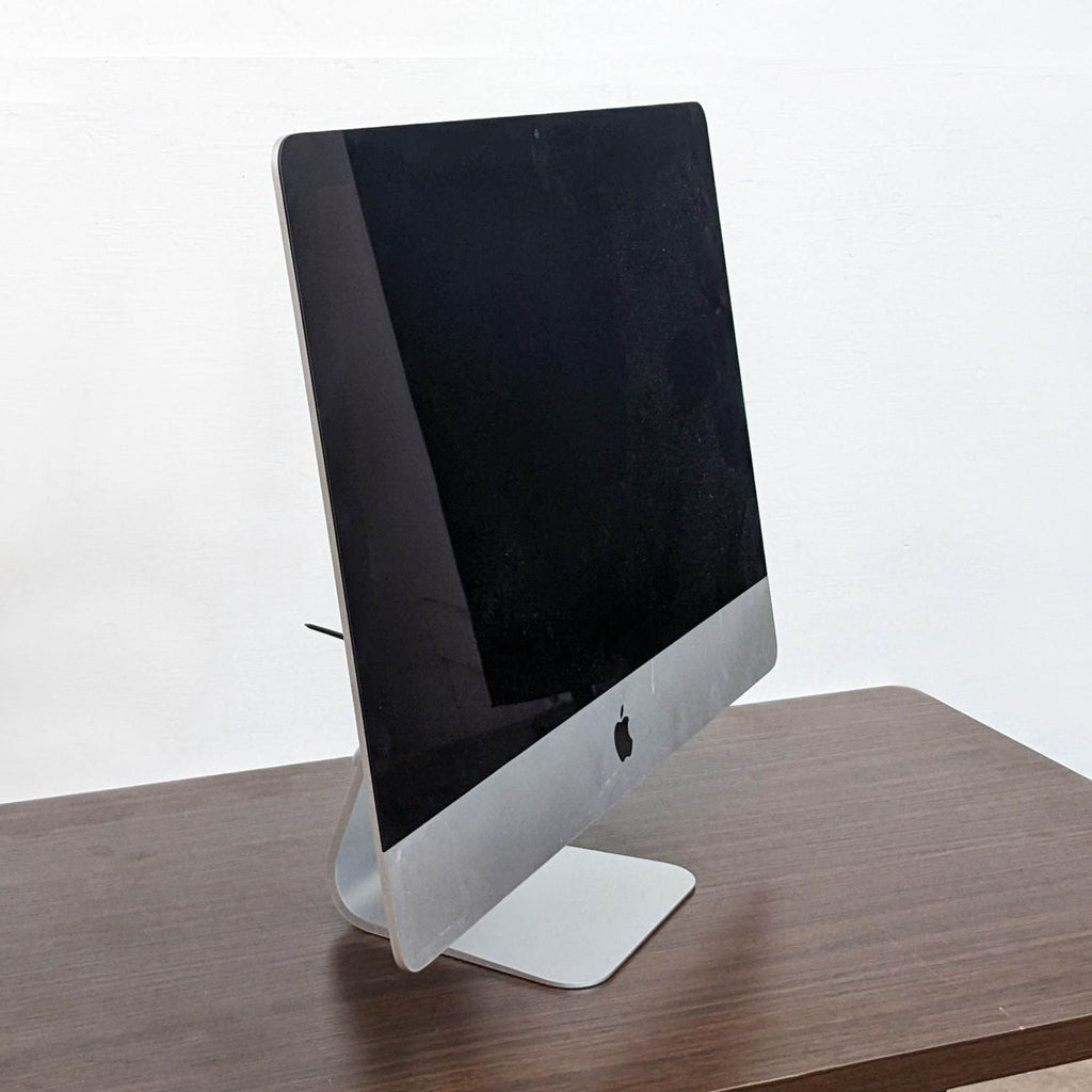 Side view of a sleek Apple monitor with a silver stand, placed on a wooden table.