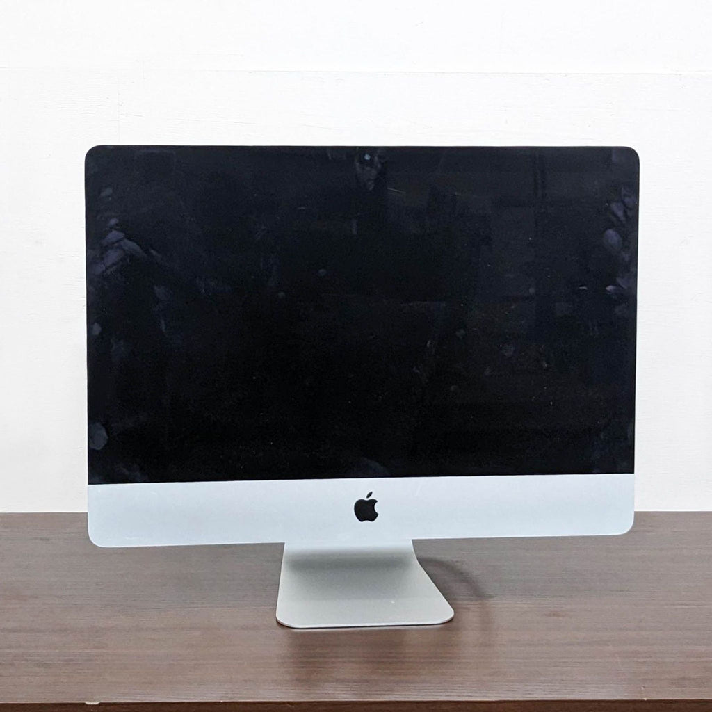 Front view of an Apple monitor with black screen, on a wooden surface.