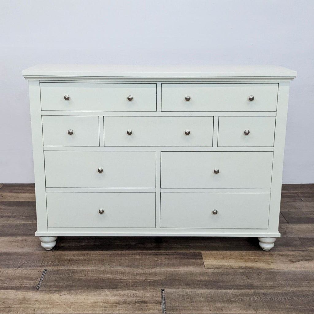 1. Front view of a white Aspen Home Cambridge “Chesser” dresser with 9 drawers and pewter hardware.  