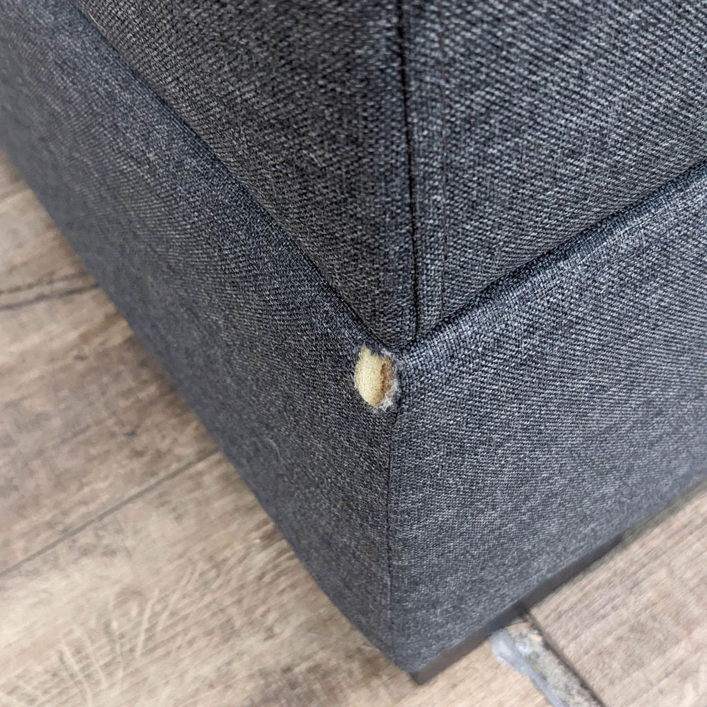 Close-up of a small tear in the fabric of a gray chaise lounge.  