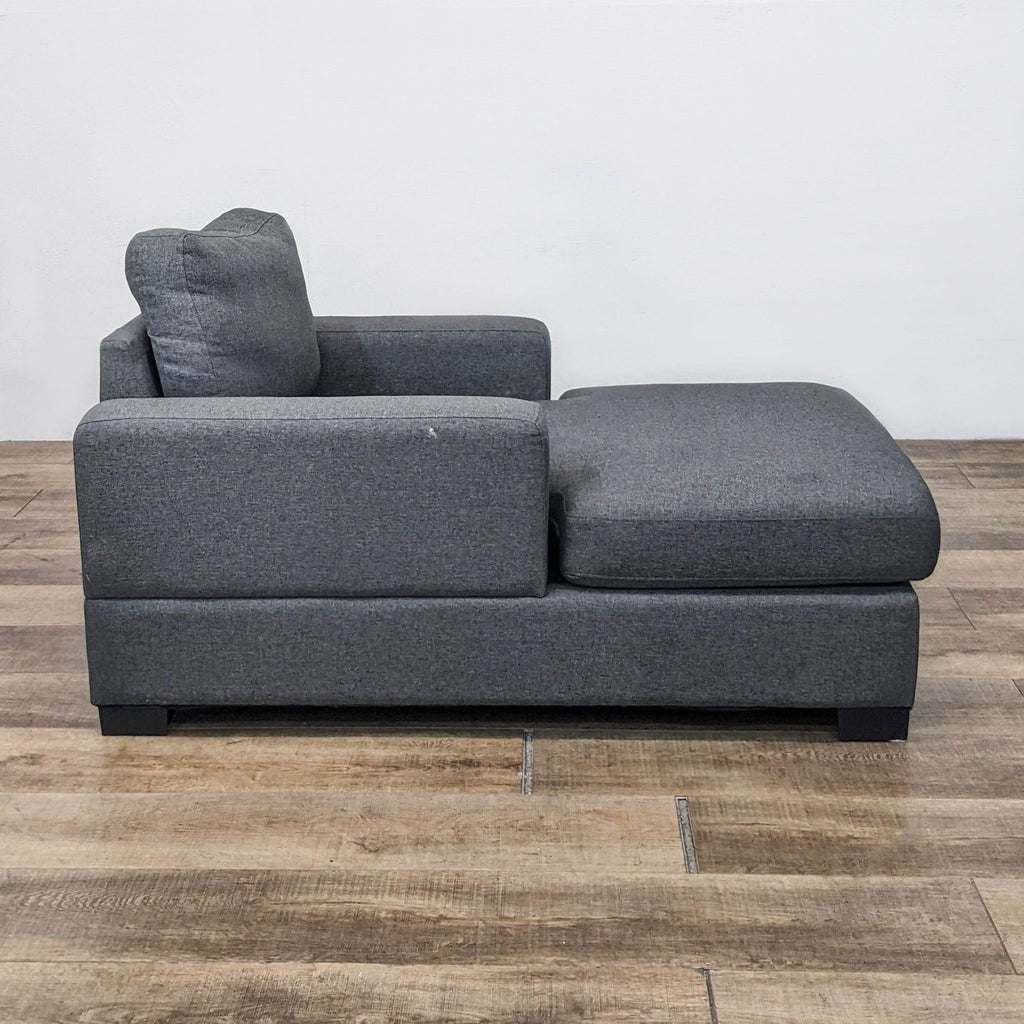 Side view of a gray plush polyester chaise lounge on wooden floor.  
