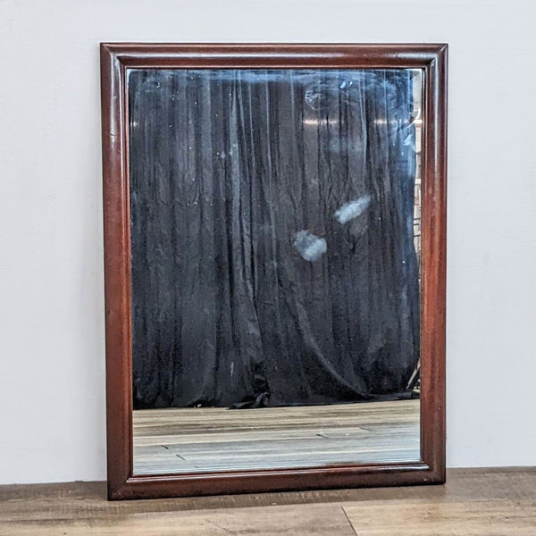 Traditional mirror with light cherry frame against a dark draped backdrop.