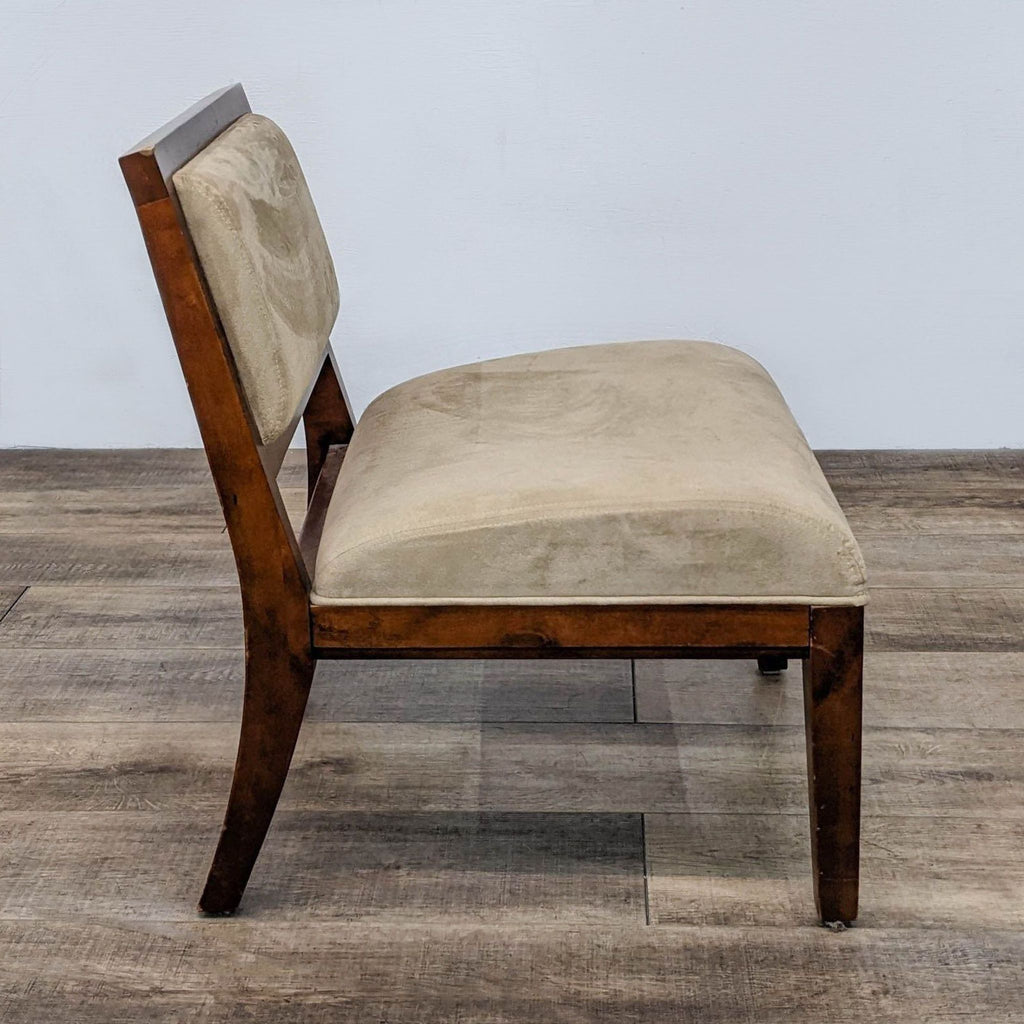 Side view of a wooden slipper chair with beige microfiber fabric on a wooden floor.