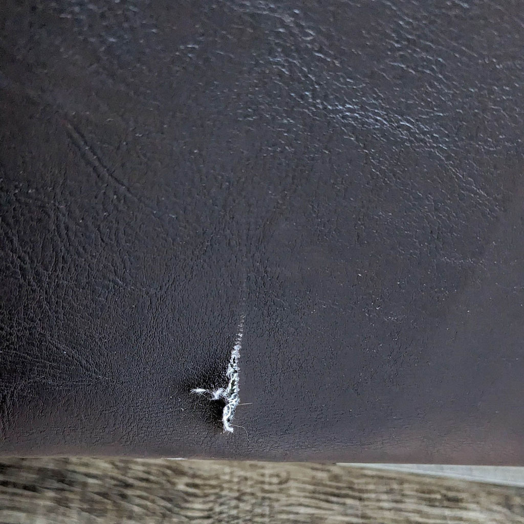 Detailed view of scratch on brown leather-look sofa surface.