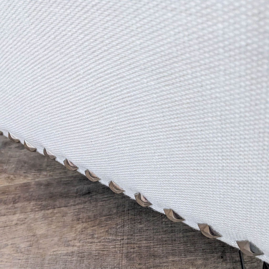Close-up of ottoman's off white fabric and nailhead trim detail.