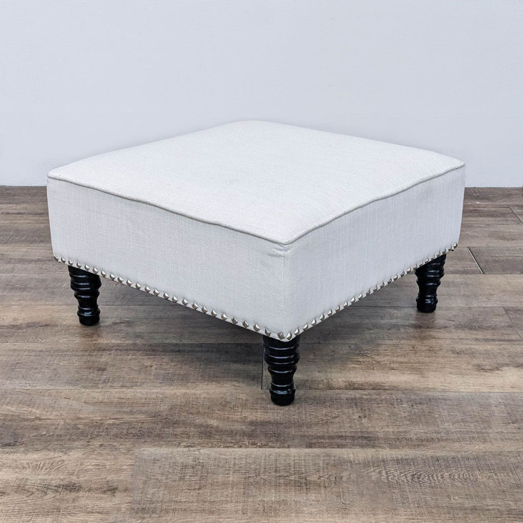 Off White ottoman with nailhead detailing and spindle legs on wood floor.