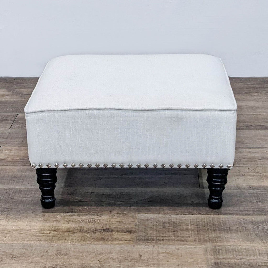 Square ottoman by Reperch with decorative nail heads and spindle feet.
