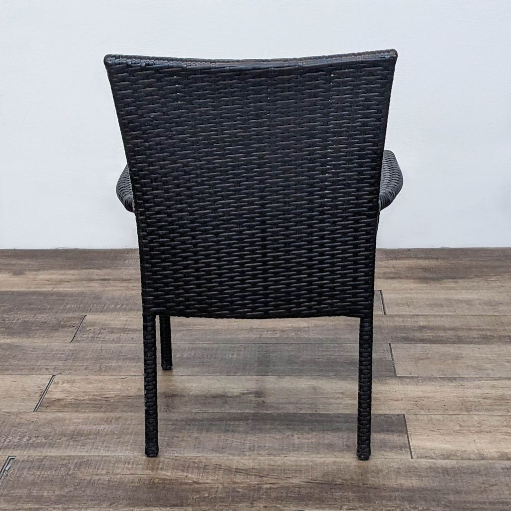 Back view of a woven plastic rattan armchair on wooden floor.