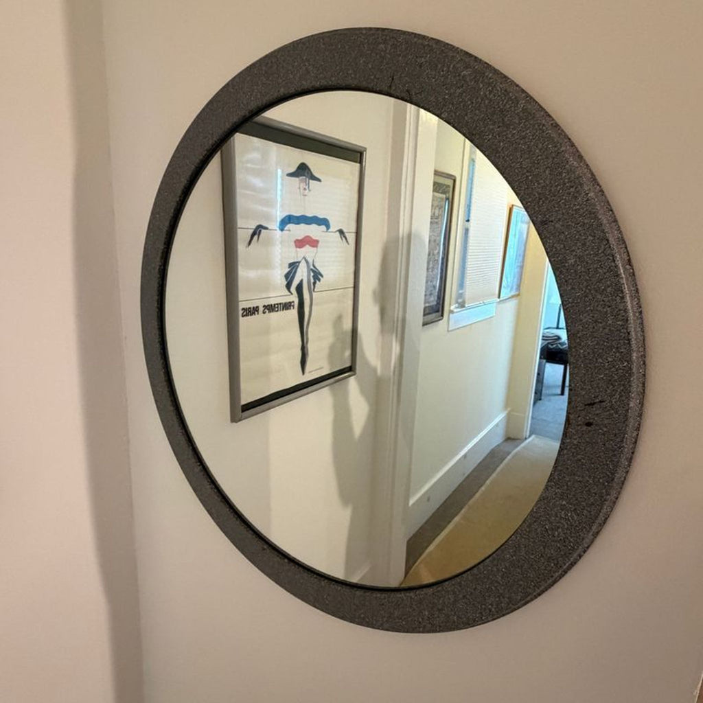 2. Circular mirror with a textured border, reflecting wall art and a hallway of a home.  