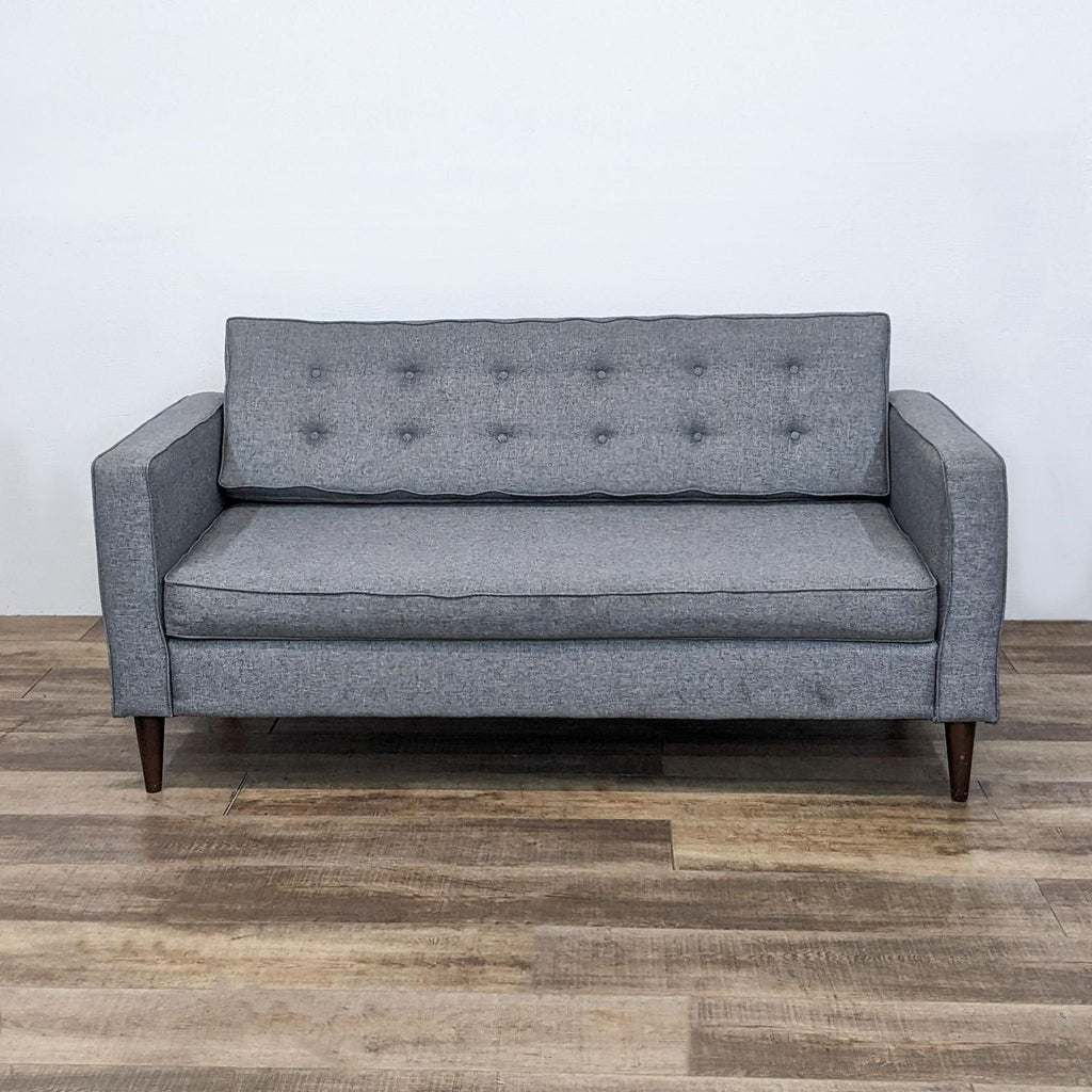 Gray tufted 3-seat sofa with narrow arms and tapered feet on wood floor.