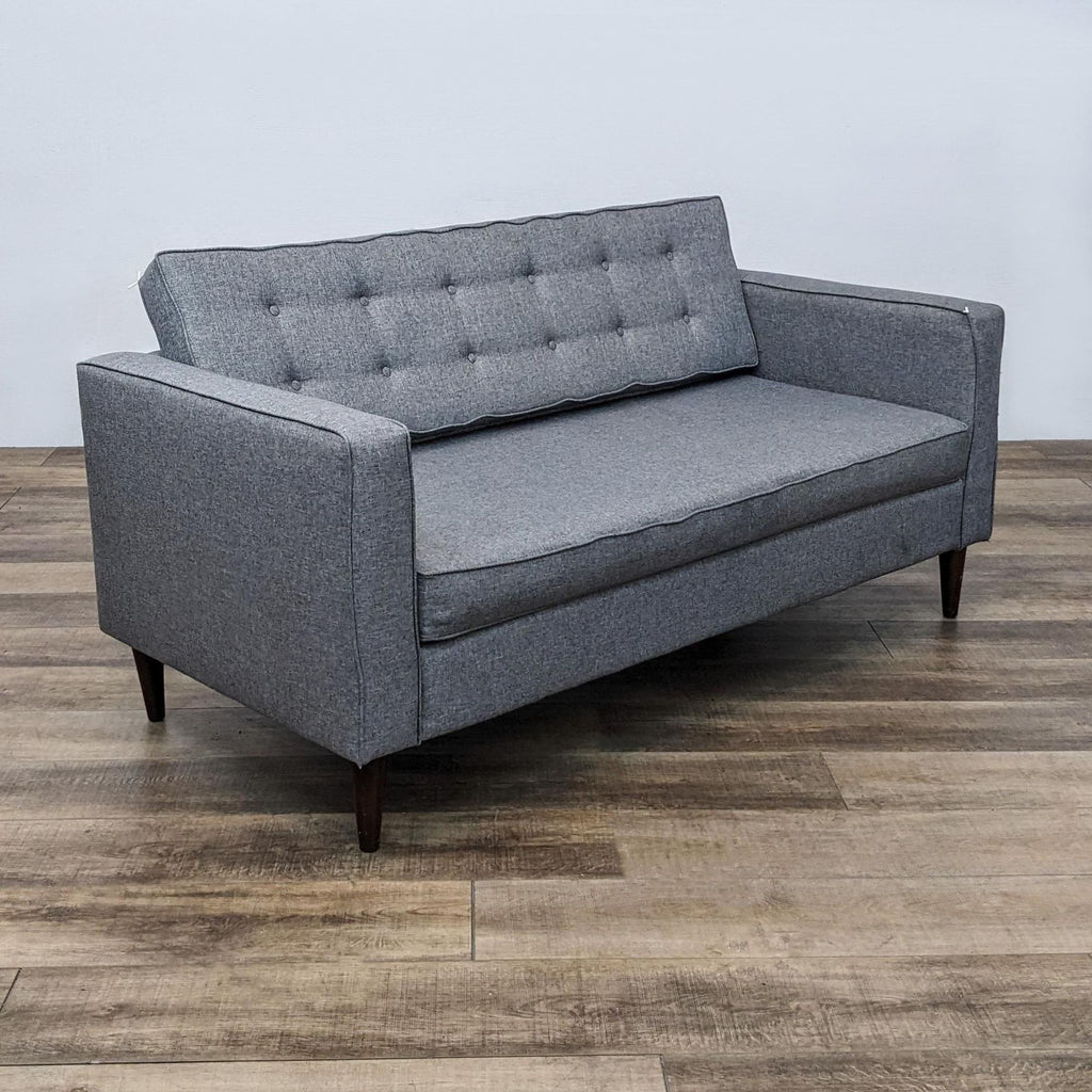 Side view of a gray 3-seat sofa with tufted back and track arms on wood flooring.
