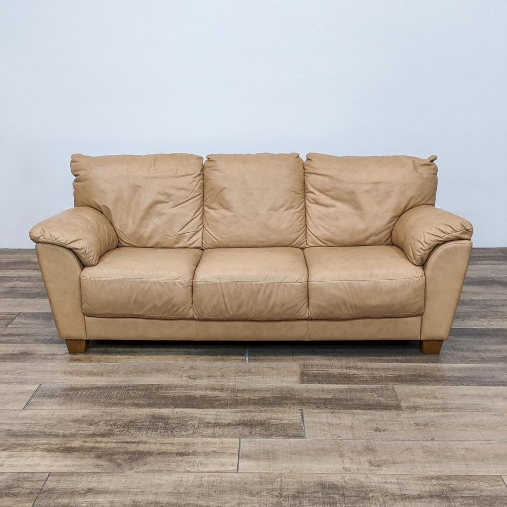 Front view of a tan leather high back sofa with pillow top arms.