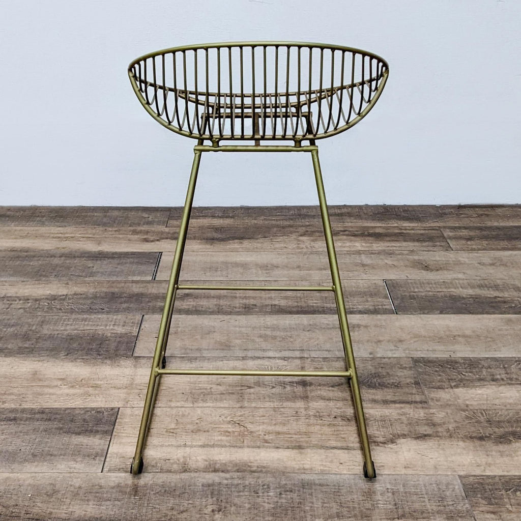 Side view of gold slat stool featuring rounded back and footrest, placed on wooden floor.