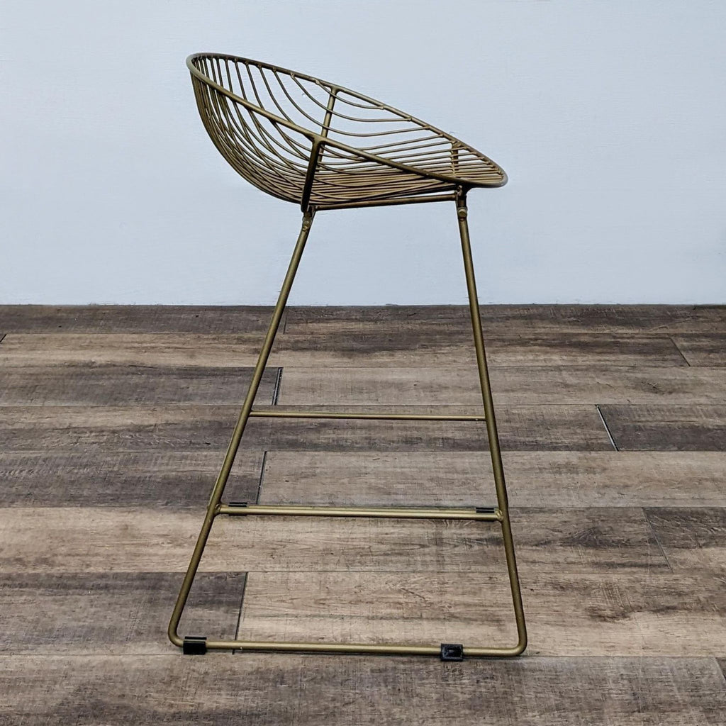 Modern gold stool with round slat back and footrest, displayed on a wooden surface.
