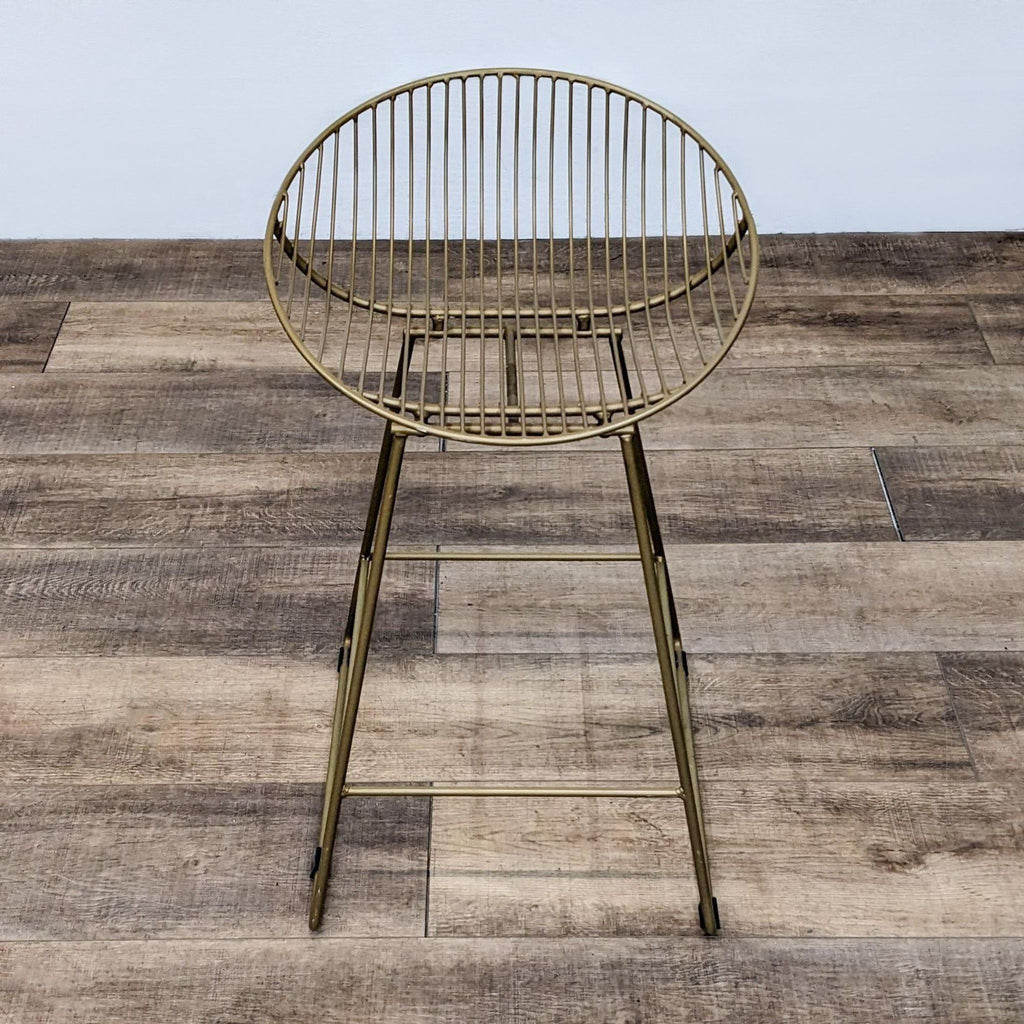 Rounded back gold stool with slat design and footrest on wooden floor.