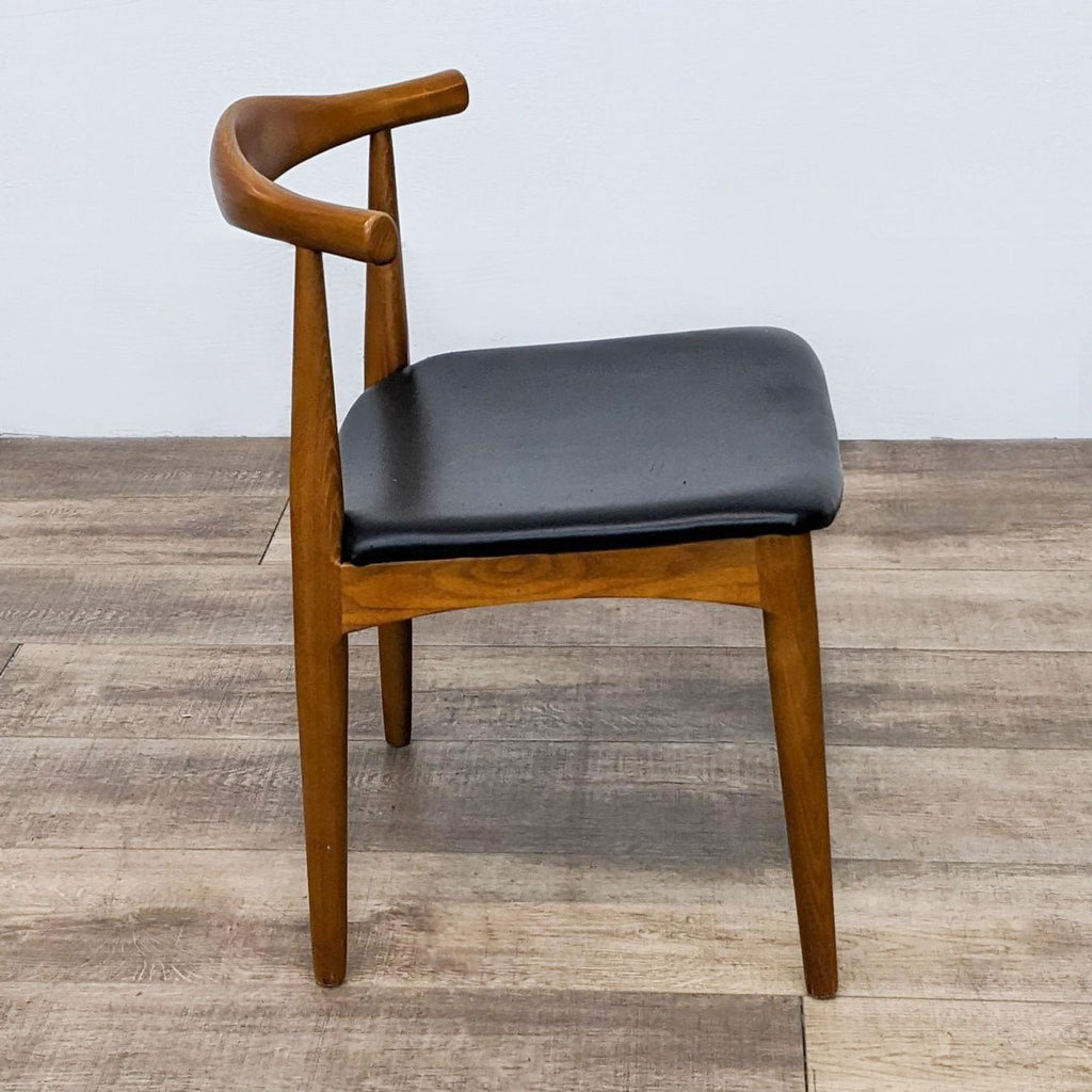 Side view of wooden dining chair with black padded seat.