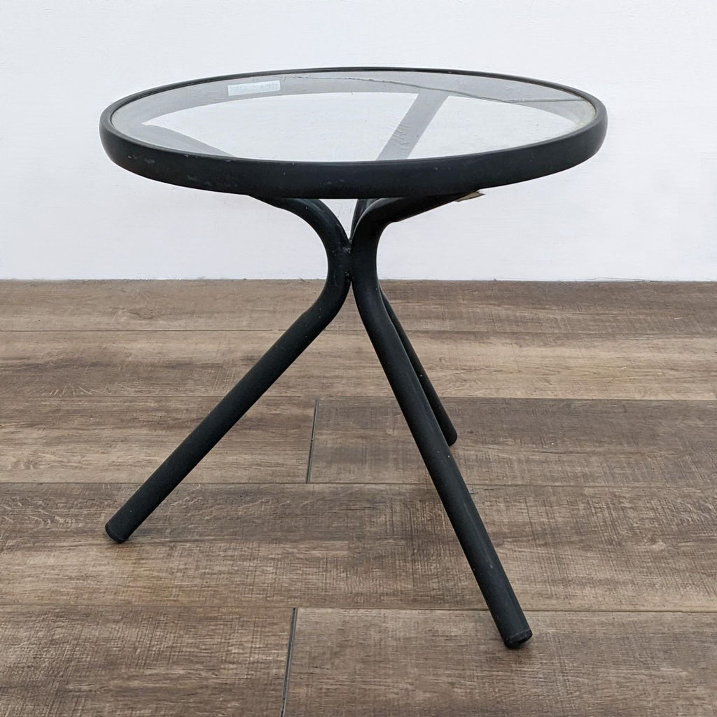 Round black aluminum table with glass top, standing on three legs.