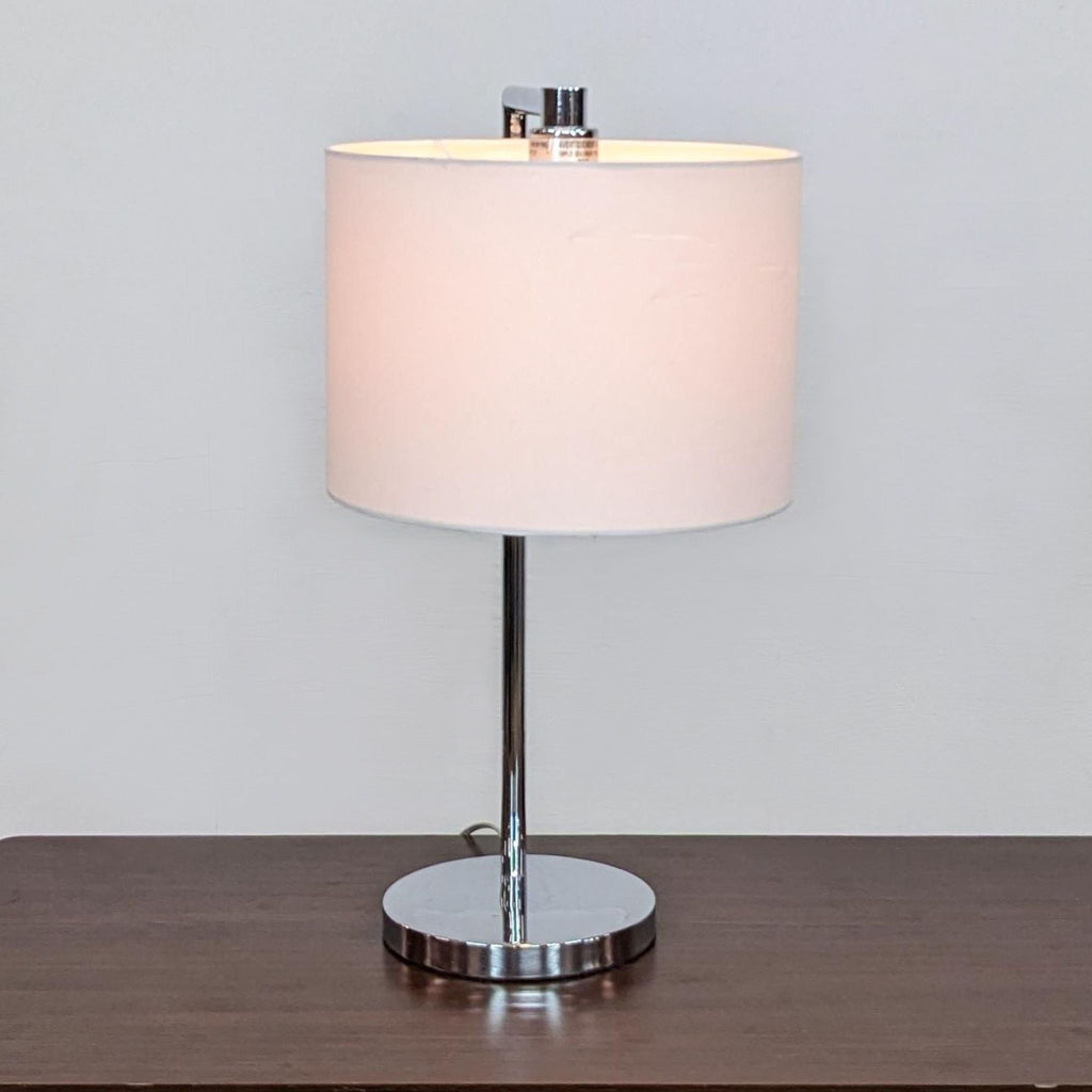 Zuo Modern table lamp with a white shade and chrome base on a wooden surface.