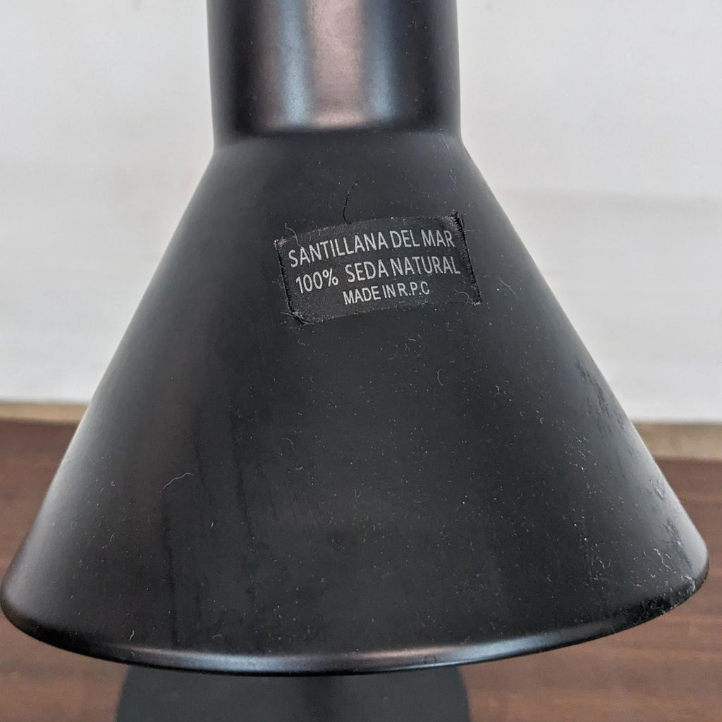 Close-up of the lamp's conical black shade with a label reading "Santillana Del Mar."