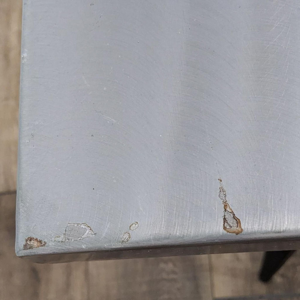 Close-up of table edge showing brushed metal texture with minor wear.