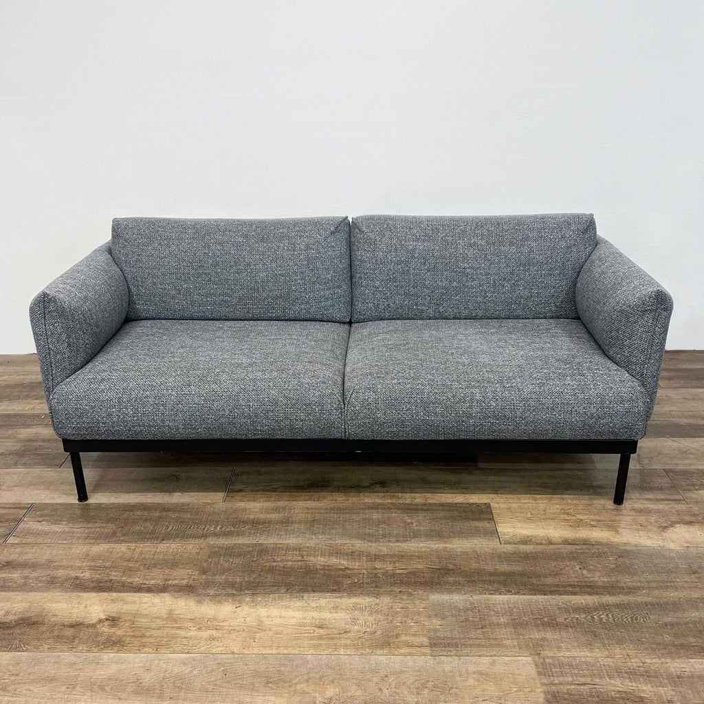Modern gray fabric loveseat with dark metal base and legs, in a minimalist design.  