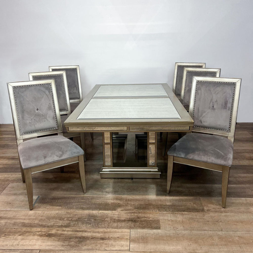 Expandable dining table with antiqued mirror panels and metallic trim, accompanied by six grey velvet chairs.