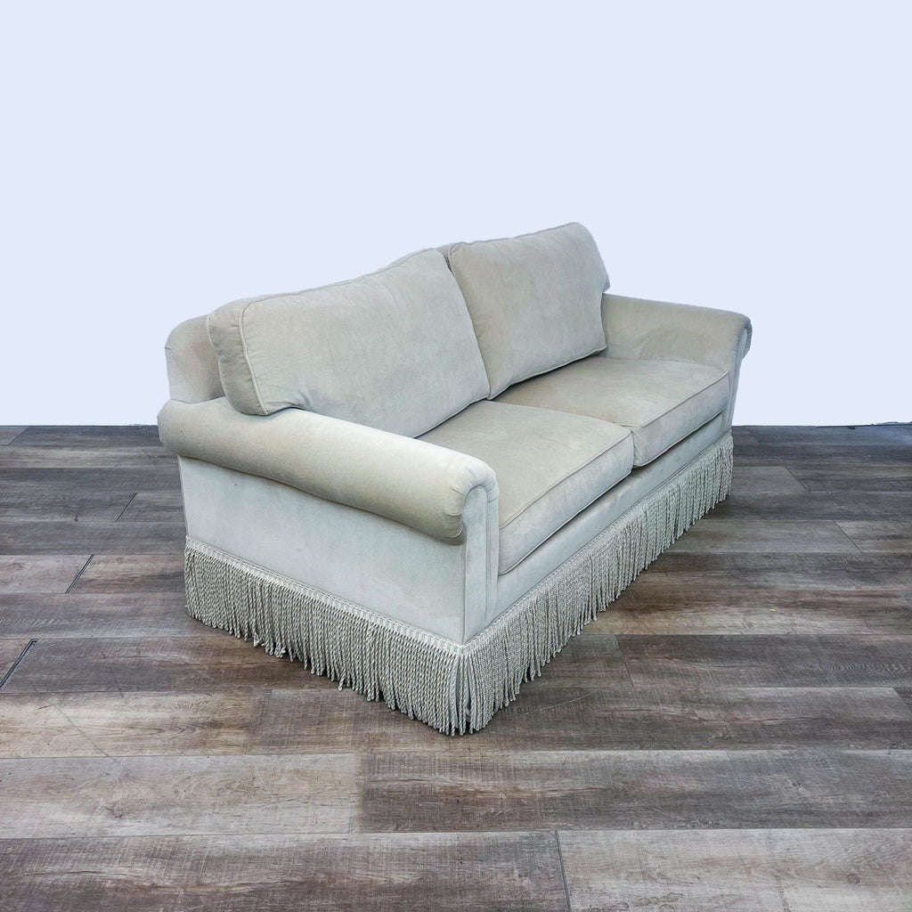 Side view of a camel fabric sofa with rolled arms and fringe trim.