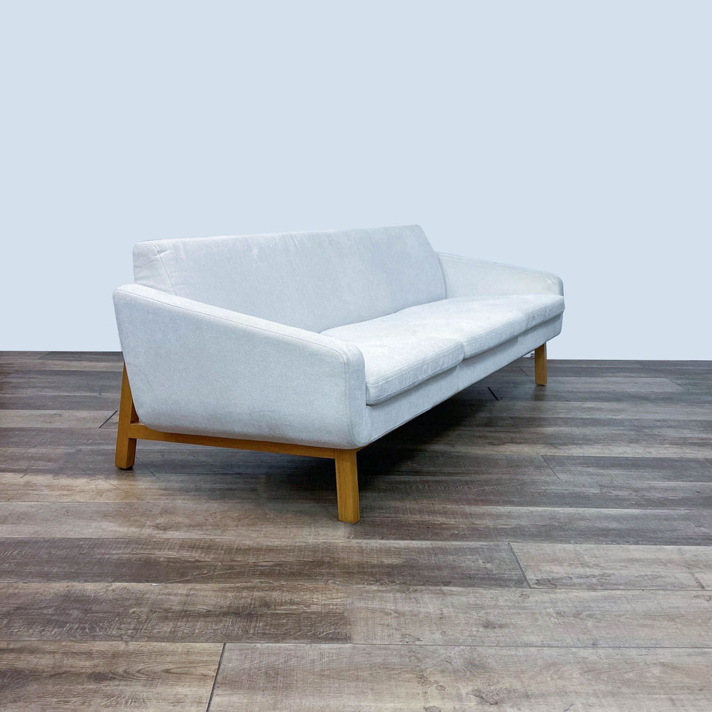 Angled view of modern HD Buttercup 3-seat sofa with clean lines, white fabric, and wooden legs.