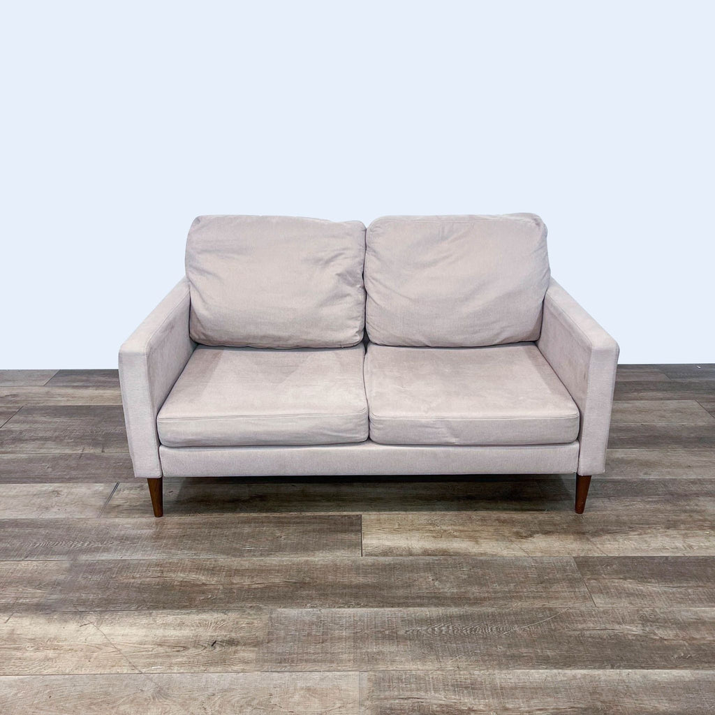 Gray loveseat with narrow arms and tapered legs on wooden floor.  