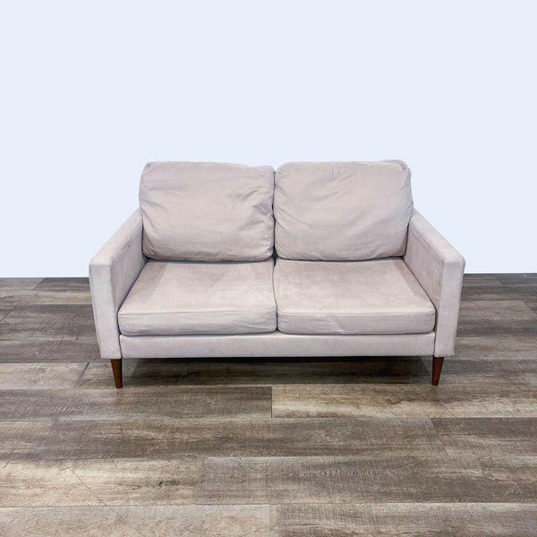 Gray loveseat with narrow arms and tapered legs on wooden floor.  