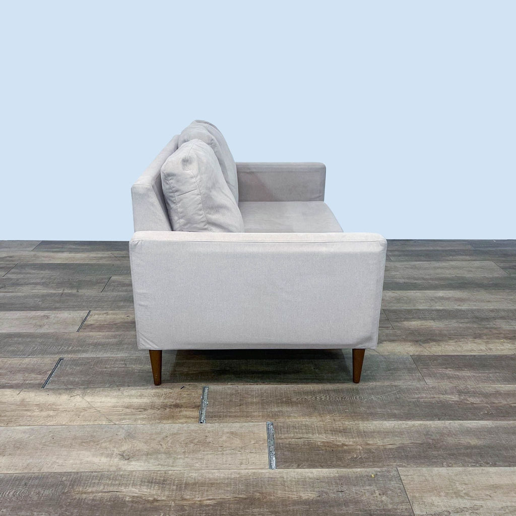 Modern loveseat with narrow arms and wooden tapered legs on a wooden floor.