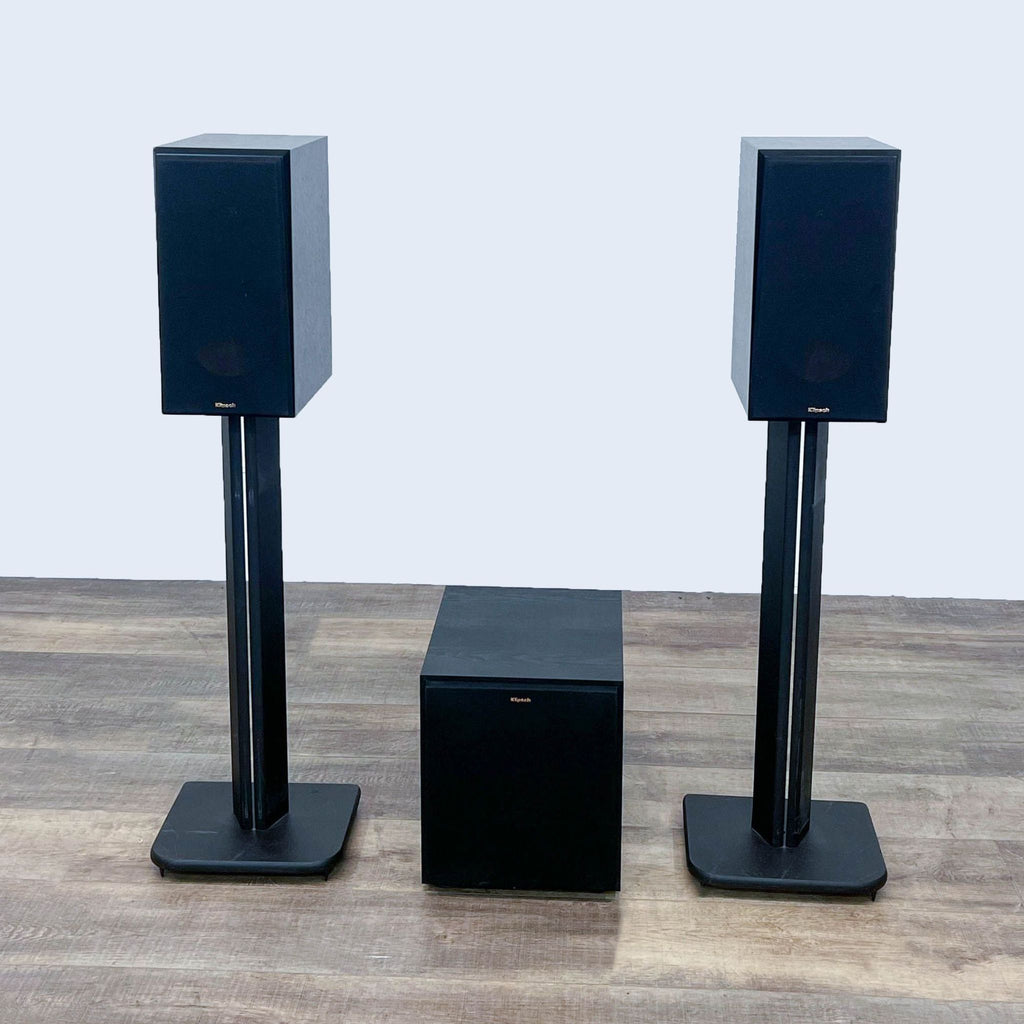 Klipsch speakers and subwoofer in black, arranged on a brown wooden floor for an audio setup.