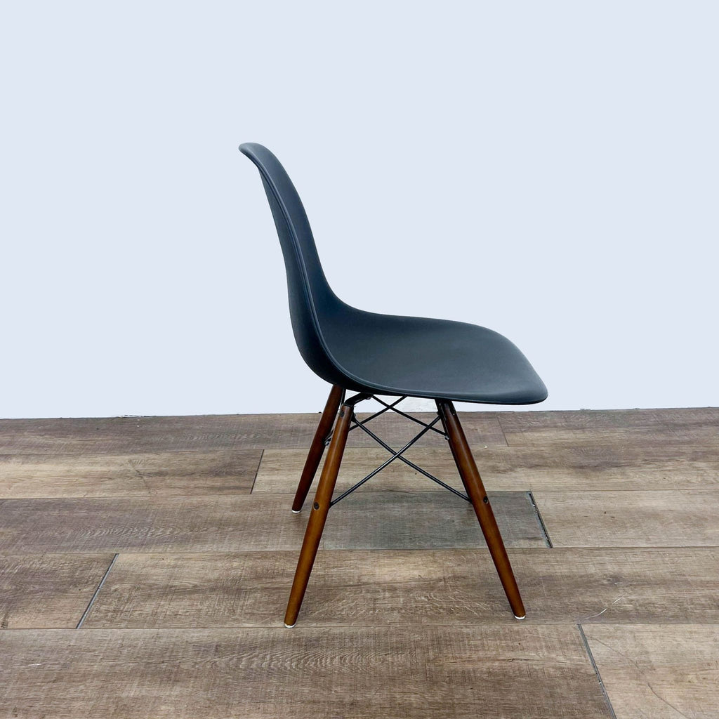 Side view of a black plastic dining chair with walnut finish legs.