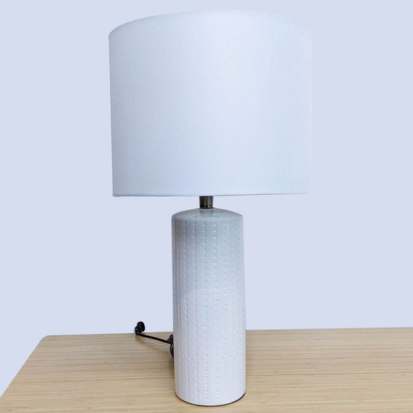 a table lamp with a white textured plastic base and a white cylinder shade.